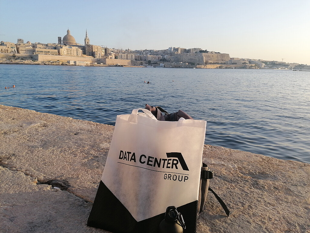 Tasche der Data Center Group im Vordergrund, Meer und Landschaft von Malta im Hintergrund