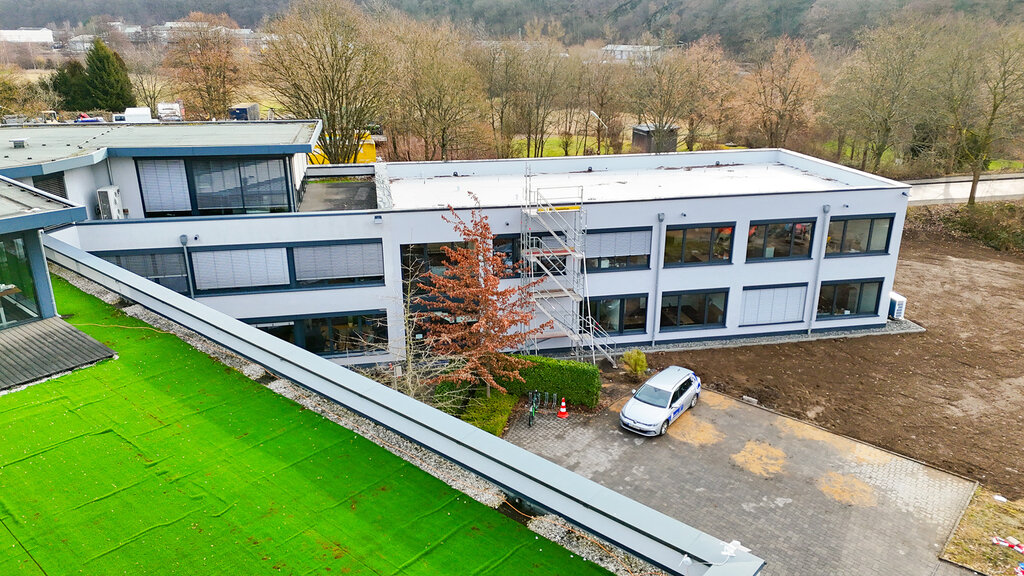 Das Firmengebäude der DCG mit grünem Kunstrasen vorne und einem weißen parkenden Auto in der Mitte