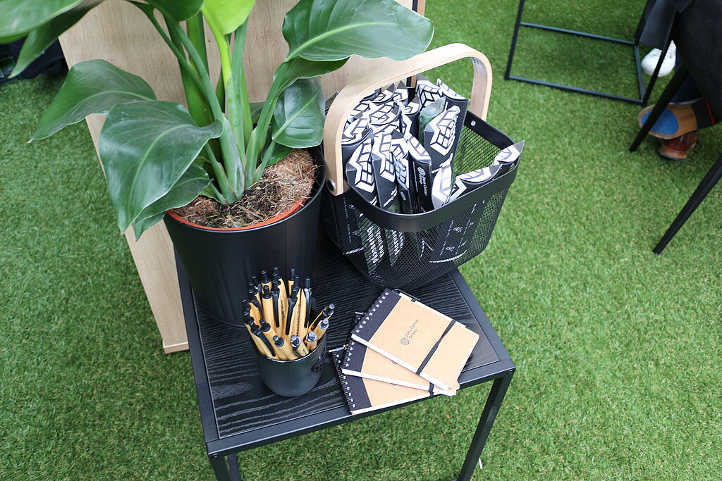 Ein Tisch, auf dem eine Pflanze, Stifte, Giveaways und Notizbücher liegen