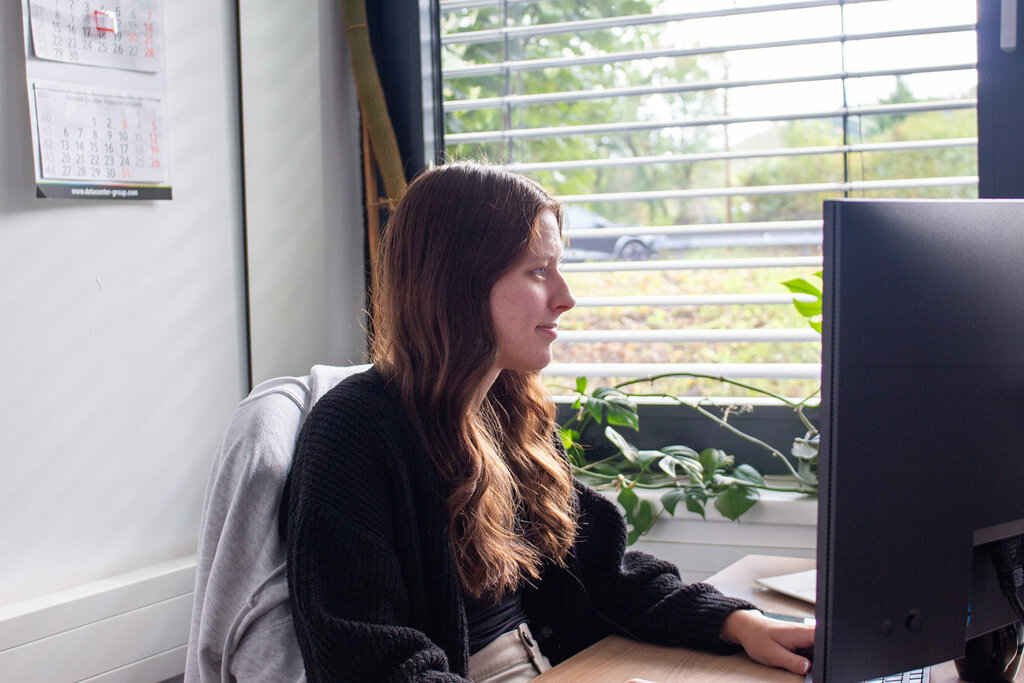 Caro sitzt am Schreibtisch und blickt auf den Monitor
