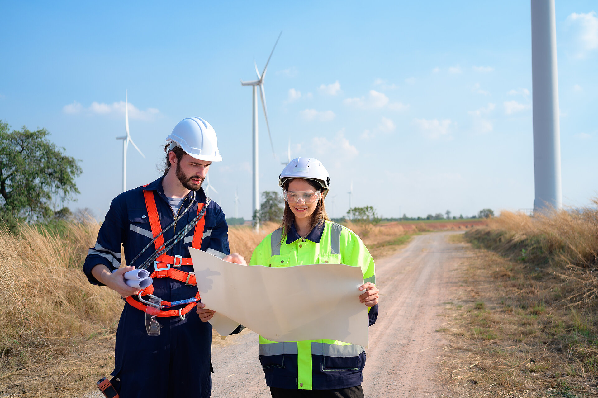 Ein Ingenieur und eine Ingenieurin schauen sich einen Plan an, im Hintergrund stehen Windturbinen