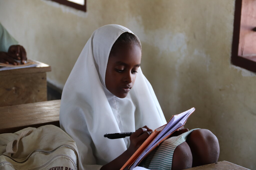 Ein Mädchen sitzt auf einem Stuhl und schreibt .