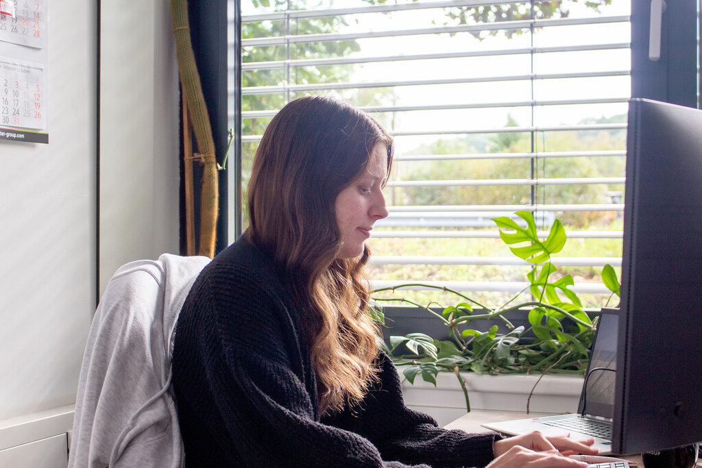 Caro sitzt am Schreibtisch und blickt auf den Monitor