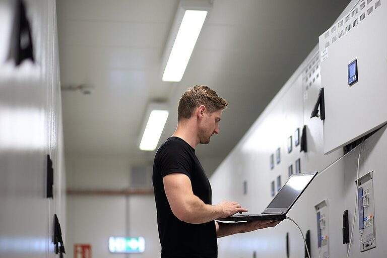 Techniker prüft Werte in einem Rechenzentrum und blickt dabei auf seinen Laptop