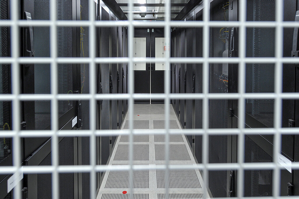 Im Vordergrund Gitter, dahinter Rechenzentrum mit Servergang und Racks
