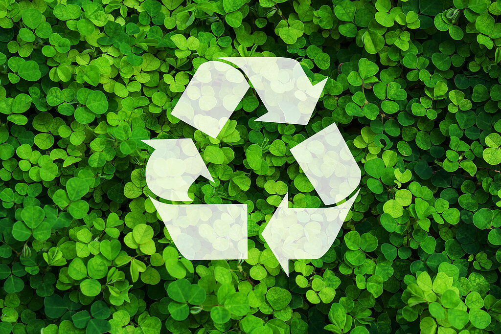 Recycling-Zeichen, im Hintergrund grüne Blätter