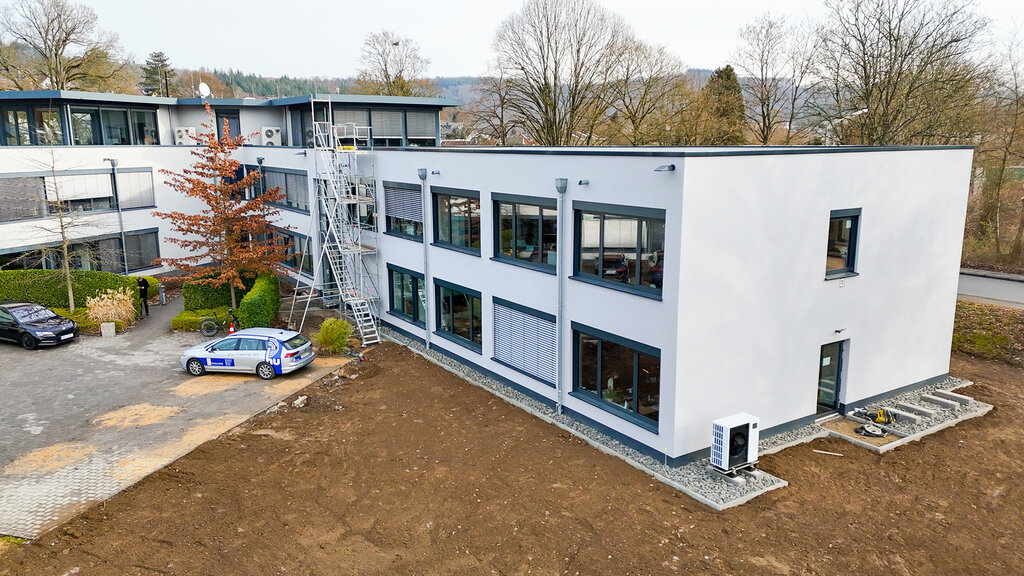 Das Firmengebäude der DCG mit Erdfläche unten in der Mitte und parkenden Autos links