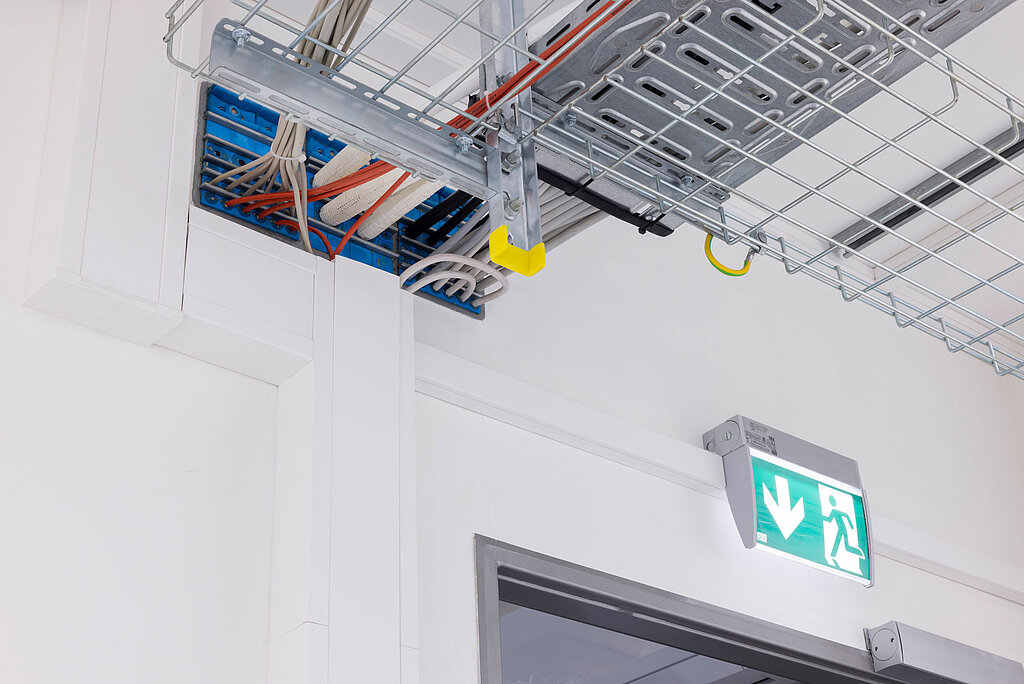 Verstrebungen an der Decke mit Kabeln und Anschlüssen, Notausgangsschild