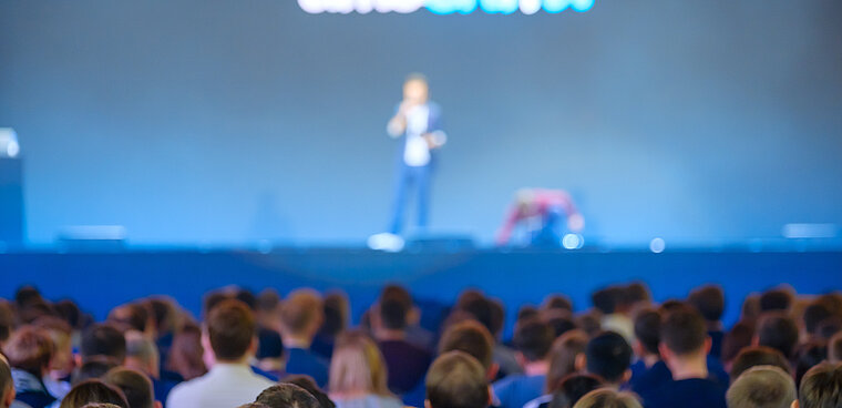 Spectators look at a stage on which a man is speaking
