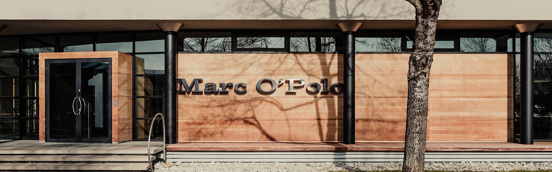 Building Marc O Polo with lettering in front, wooden facade, tree and street in front of it