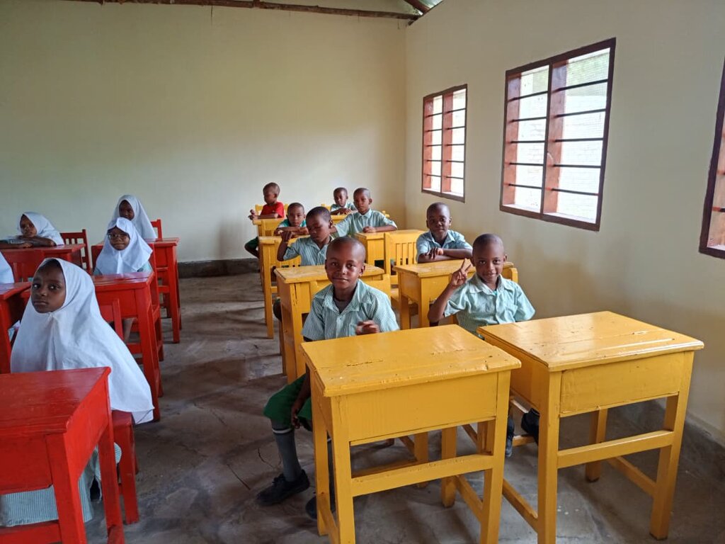 Kinder sitzen im Klassenraum an bunten Schultischen und lernen gemeinsam