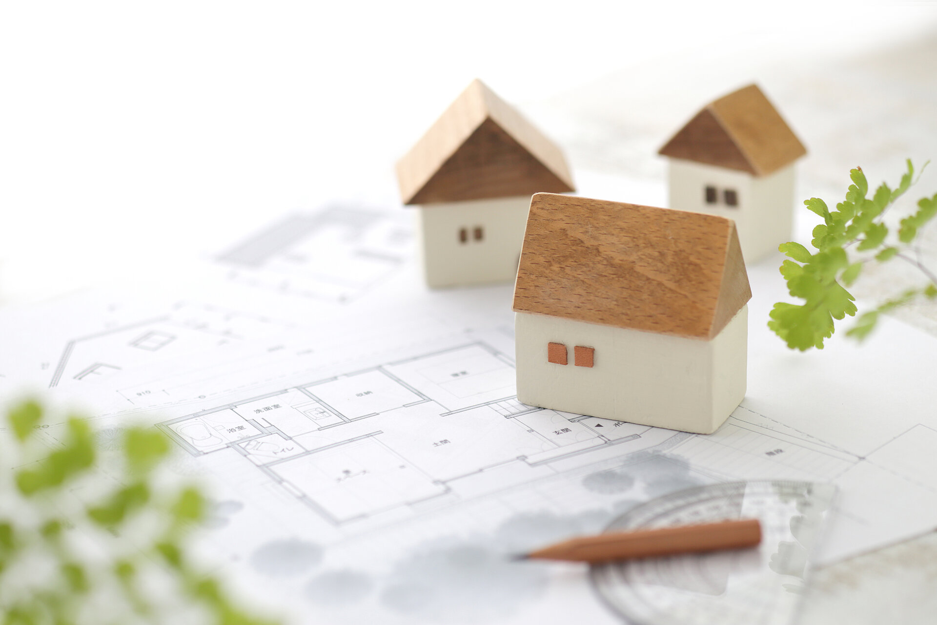 Baupläne mit Miniaturhäusern aus Holz darauf, seitlich grüne Blätter