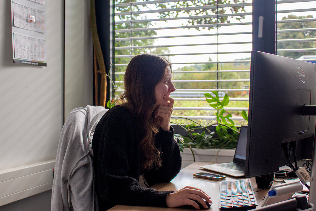 Caro sitzt am Schreibtisch und blickt auf den Monitor