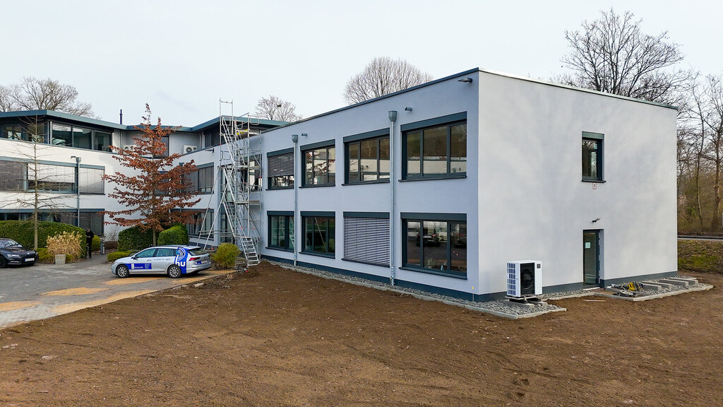 Das Firmengebäude der DCG mit Erdfläche unten in der Mitte und parkenden Autos links