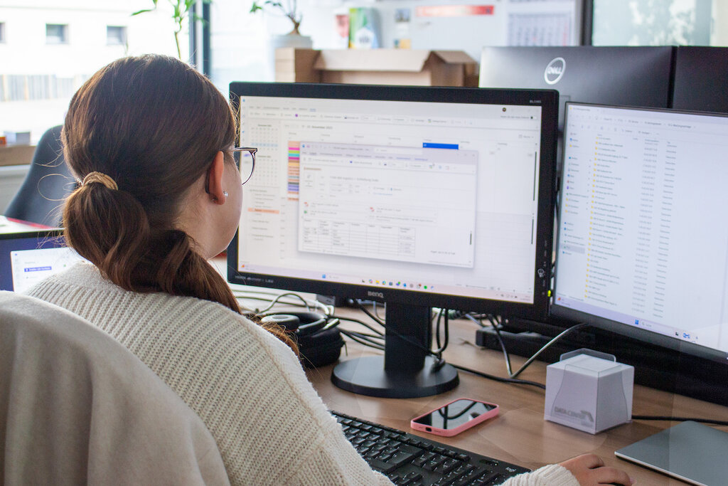 Nele am Schreibtisch sitzend und auf den Monitor blickend, Rückansicht