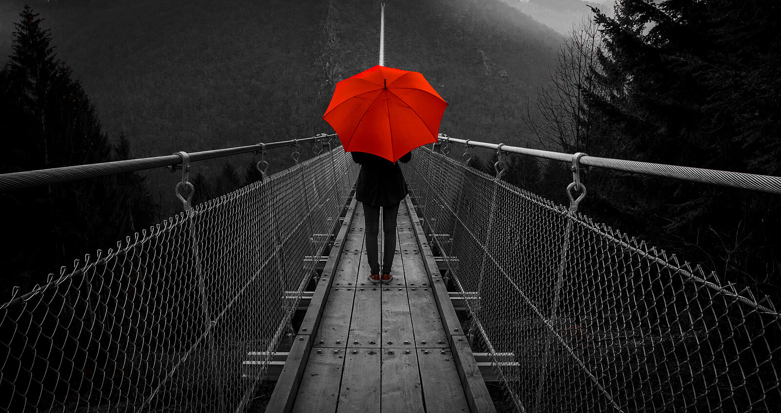 Frau mit rotem Regenschirm auf einer Hängebrücke