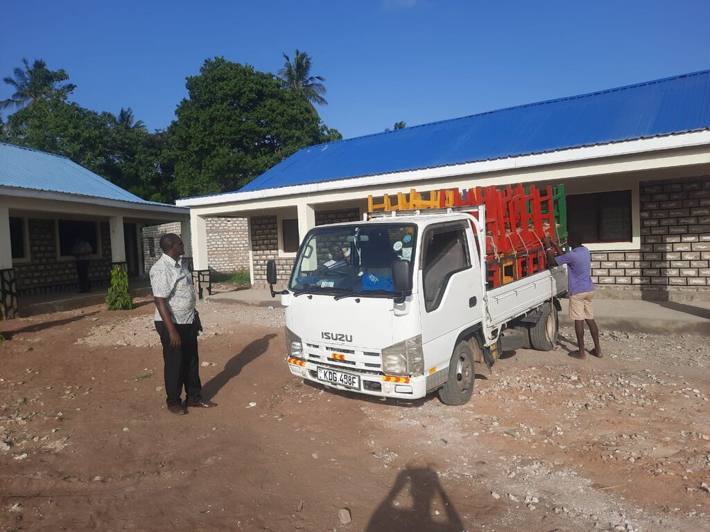 Transporter mit bunten Schultischen vor dem Schulgebäude, Beginn des Entladens