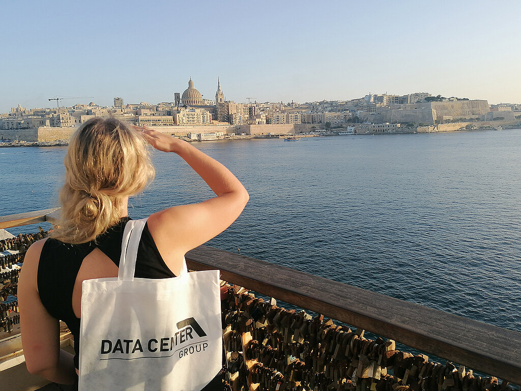Auszubildende mit dem Blick auf das Meer und eine Landschaft auf Malta mit einer Tasche der Data Center Group am Arm