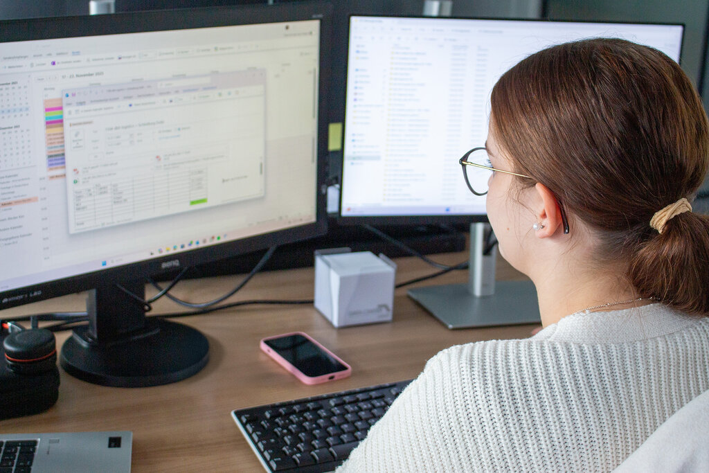 Nele am Schreibtisch sitzend und auf den Monitor blickend, Rückansicht