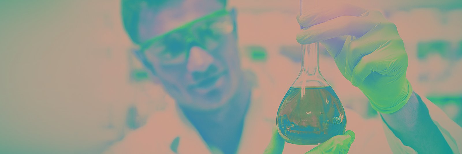 Chemikant mit Sicherheitsbrille, und Handschuhen, der ein mit einer grünen Flüssigkeit gefülltes Glas hält