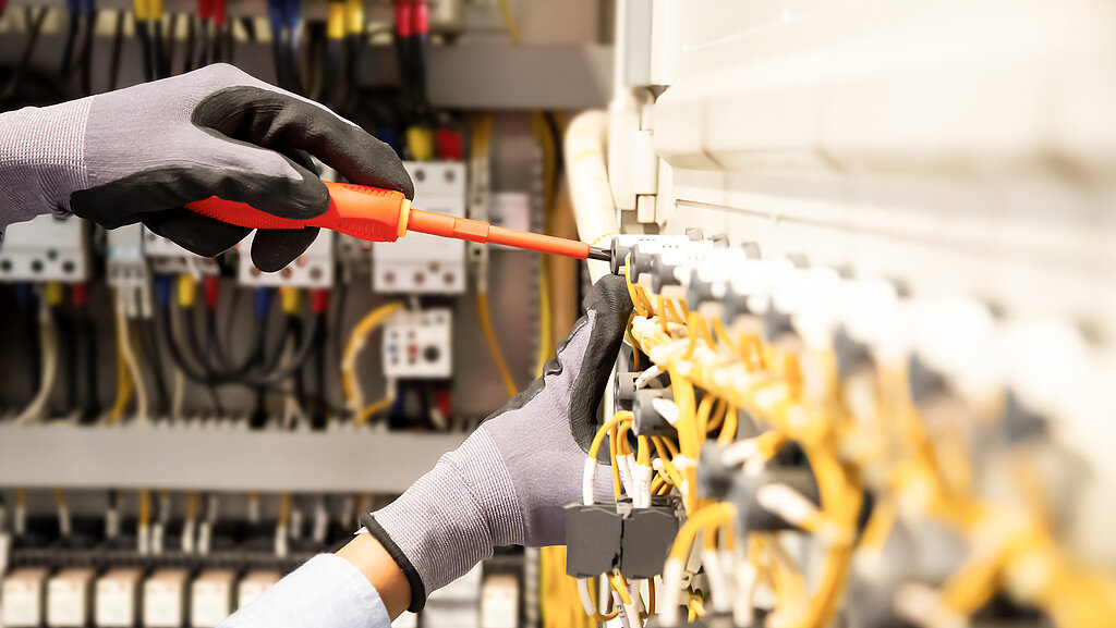 A person wearing gloves carries out an electrical installation using a screwdriver