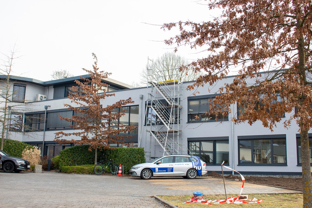 Das Firmengebäude der DCG mit Bäumen und Autos davor