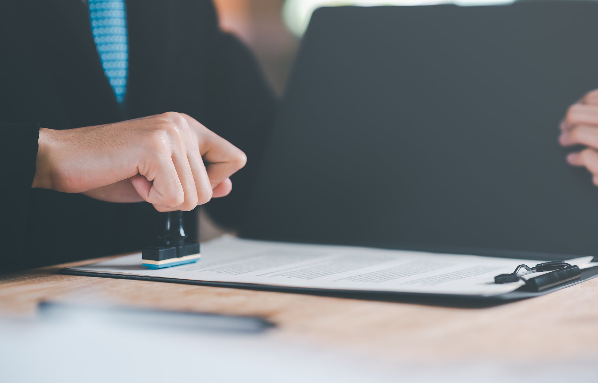 Zwei Personen sitzen an einem Schreibtisch, eine Person stempelt ein Dokument ab