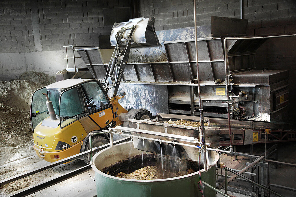Ein Bagger, der Ton in eine Maschine gibt. Ein großer Behälter voller Ton, der bewässert wird