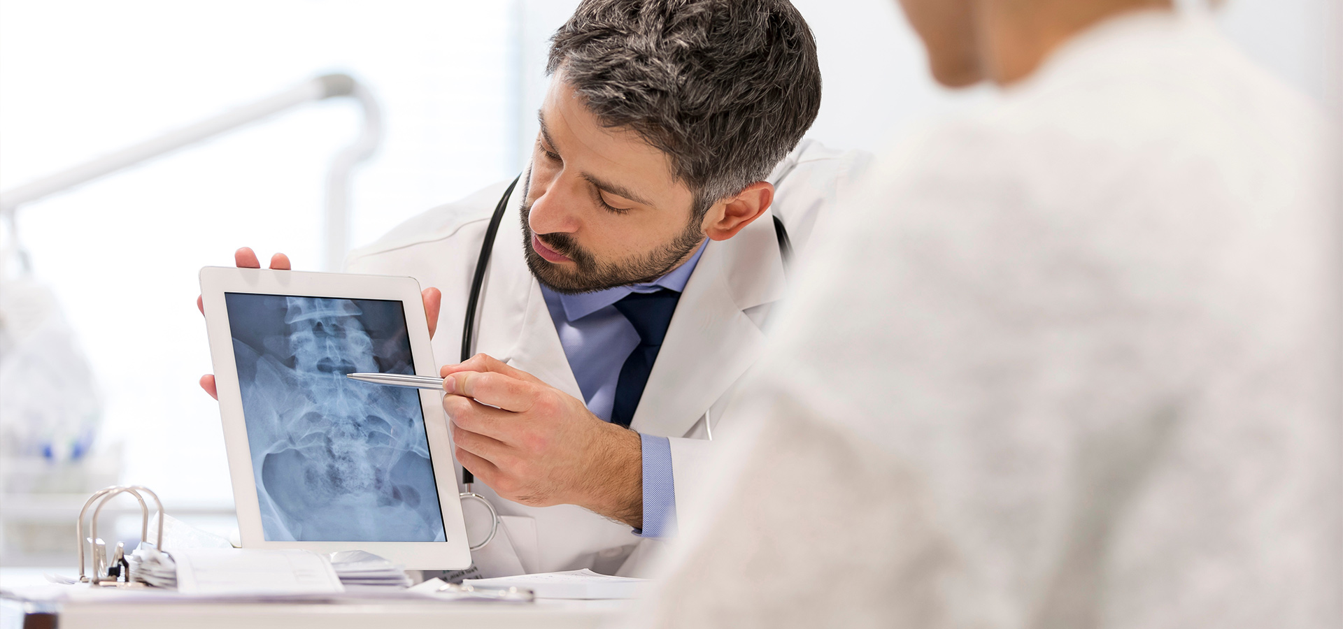 A doctor shows a patient an X-ray image on a tablet.