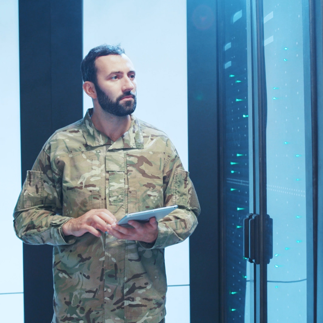 Mann in Militäruniform hält ein Tablet und läuft durch ein Rechenzentrum