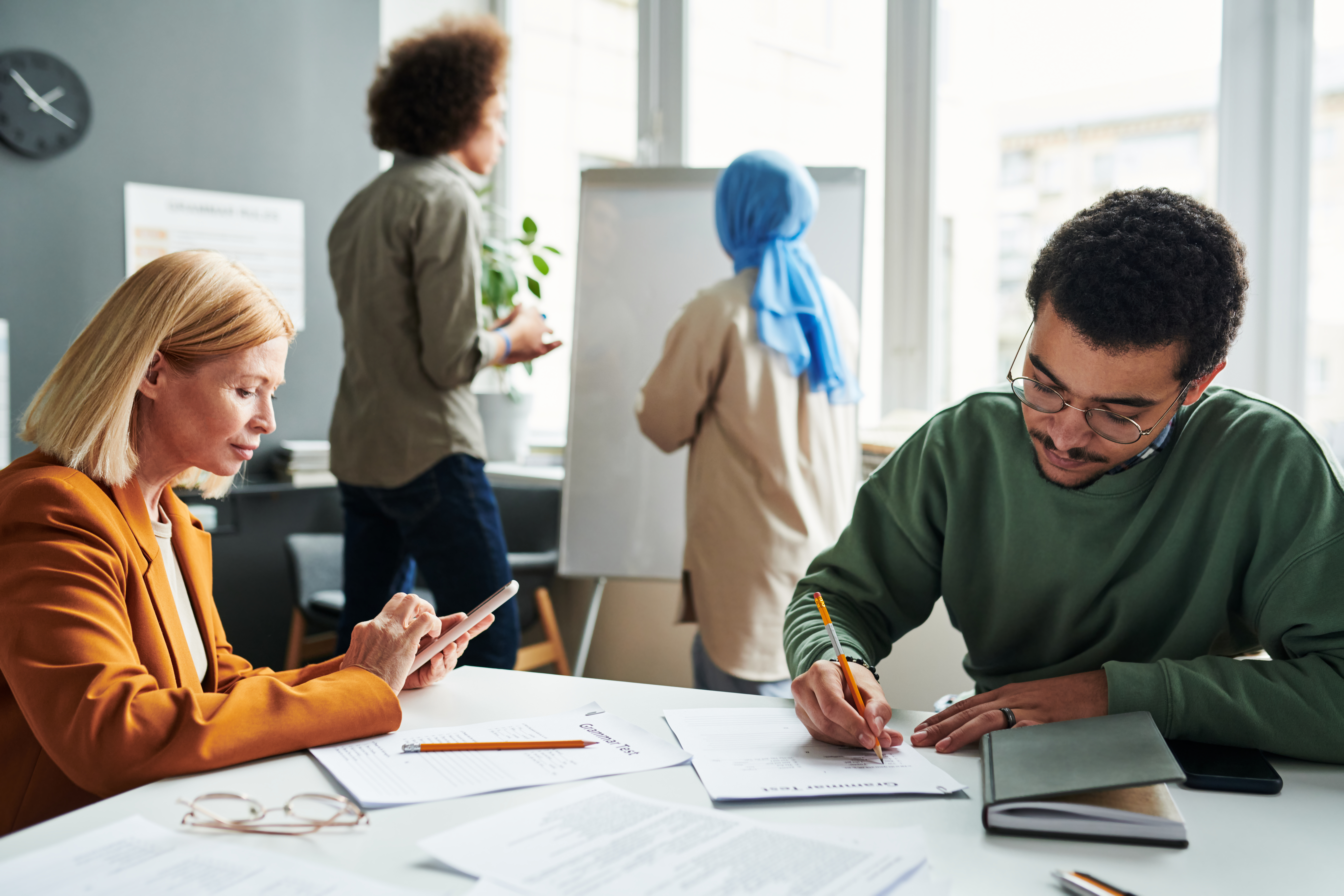 Vier Menschen sind in einem Büro, 2 stehen, 2 sitzen.