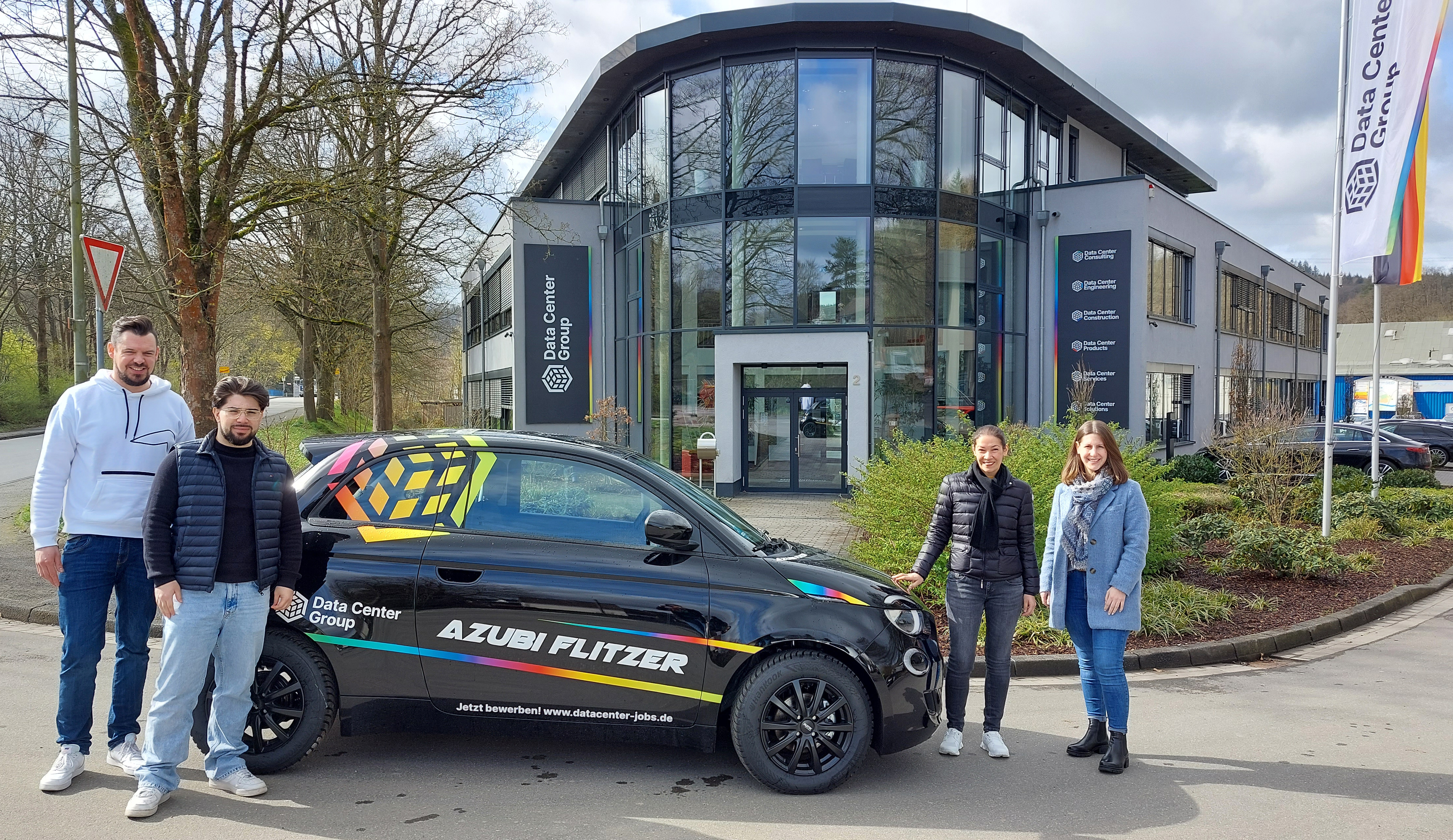 Der Azubiflitzer vor dem Hauptgebäude der DCG zusammen mit einem Azubi, dem Fuhrparkmanager, der Personalchefin und der Azubi-Beauftragten