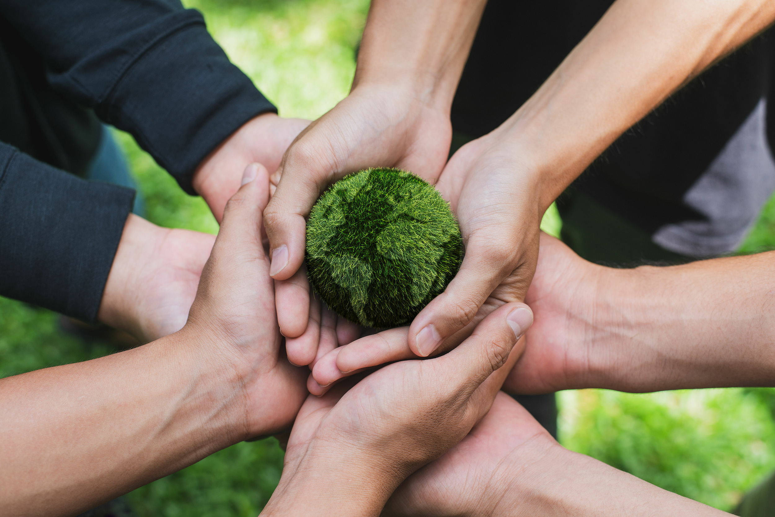 Several hands hold a small miniature earth in green