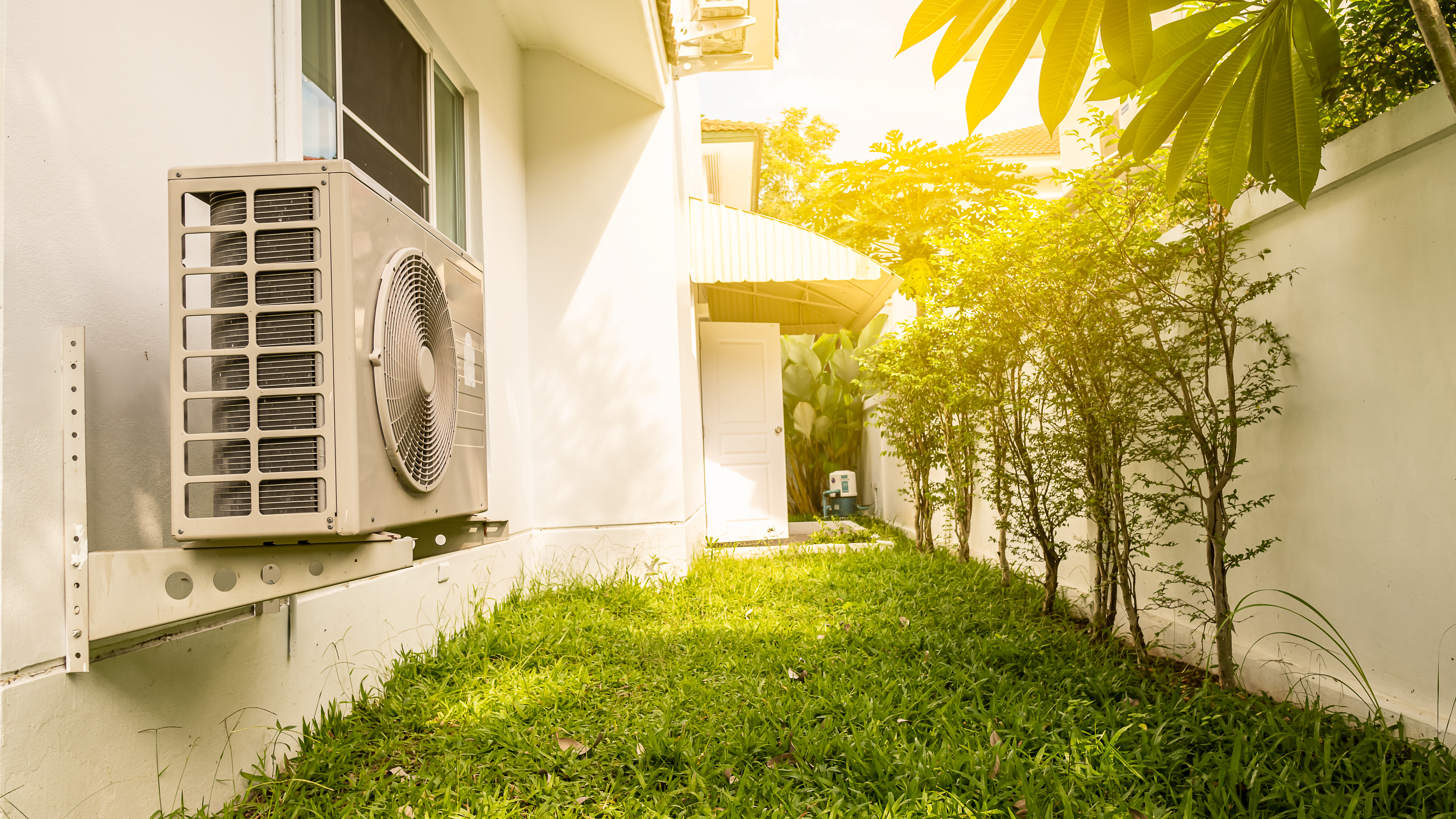 Kühlelement an einem Haus, daneben eine Wiese und Bäume