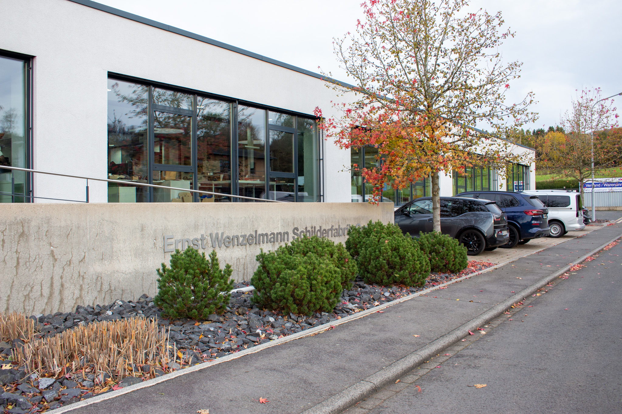 Firmengebäude der Wenzelmann Schilderfabrik mit Sträuchern und Autos im Vordergrund