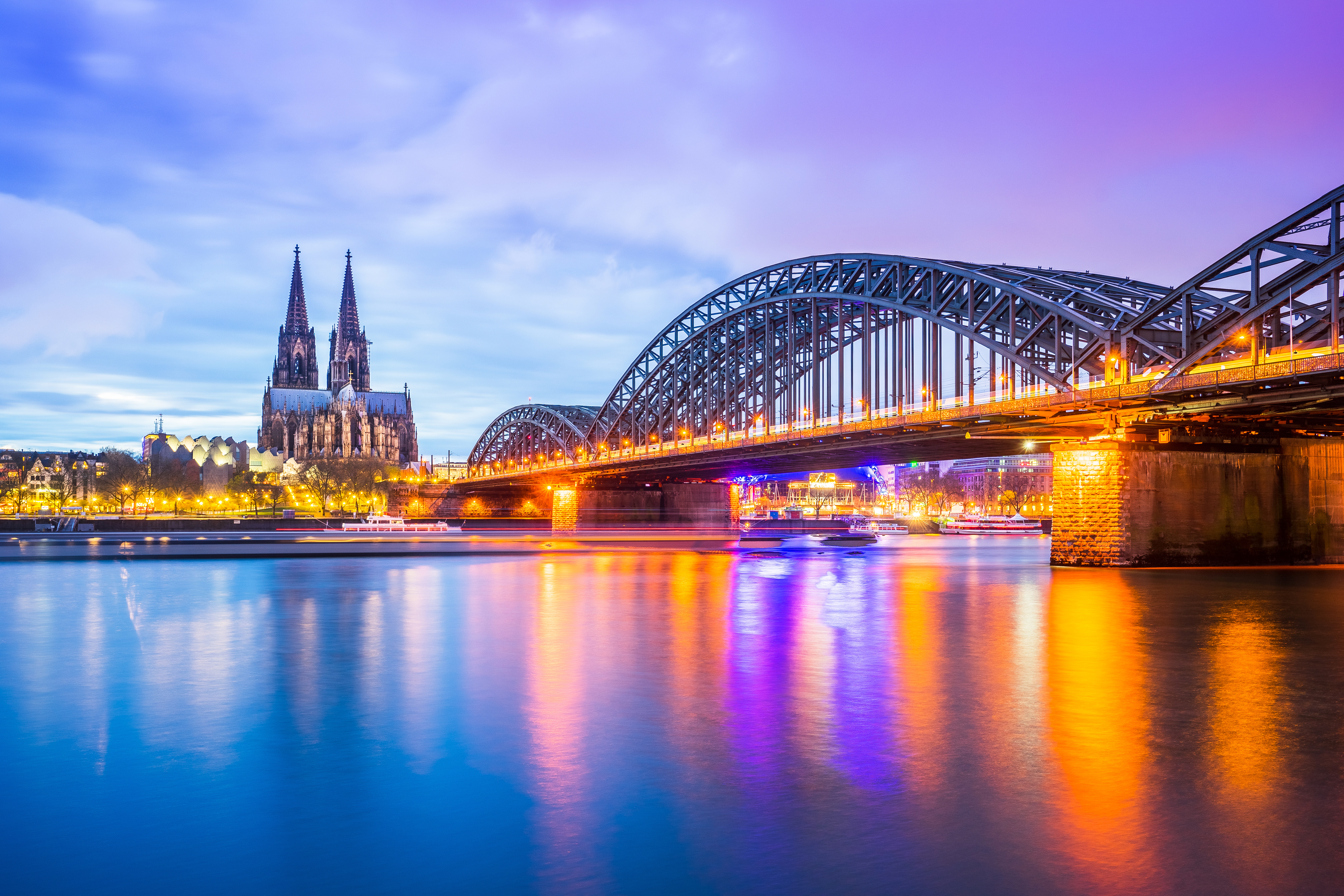 Cologne skyline at dusk, with the Rhine and Hohenzollern Bridge in the foreground and Cologne Cathedral in the background